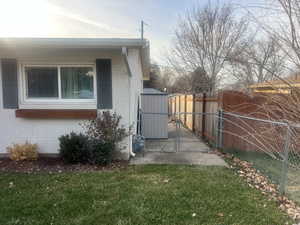 View of side of home featuring brick siding, a gate, and a storage unit