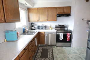Kitchen featuring stainless steel appliances, light countertops, wood finish cabinetry, and a textured wall