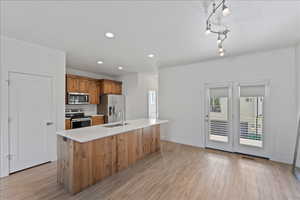 Kitchen featuring wood finish cabinets, stainless steel appliances, an island with sink, light wood-type flooring, and light stone counters
