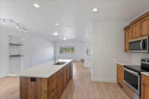 Dual tone kitchen featuring stainless steel appliances, light wood-type flooring, an island with sink, recessed lighting, and open floor plan