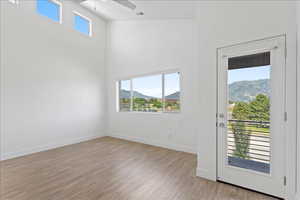 Unfurnished room featuring a mountain view, healthy amount of natural light, light wood-type flooring, a high ceiling, and a ceiling fan