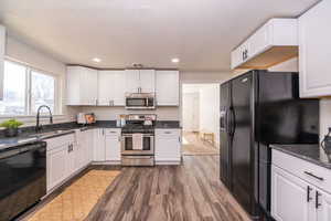 Kitchen with black appliances, white cabinets, dark wood finished floors, and recessed lighting