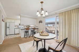 Dining room with light colored carpet, ornamental molding, and a chandelier