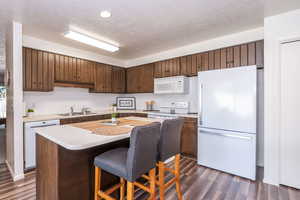 Kitchen featuring white appliances, a center island, light countertops, a breakfast bar area, and dark wood finish cabinetry