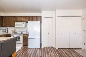 Kitchen with white appliances, light countertops, dark wood-type flooring, and dark wood finish cabinetry. Laundry in large bifold doors.
