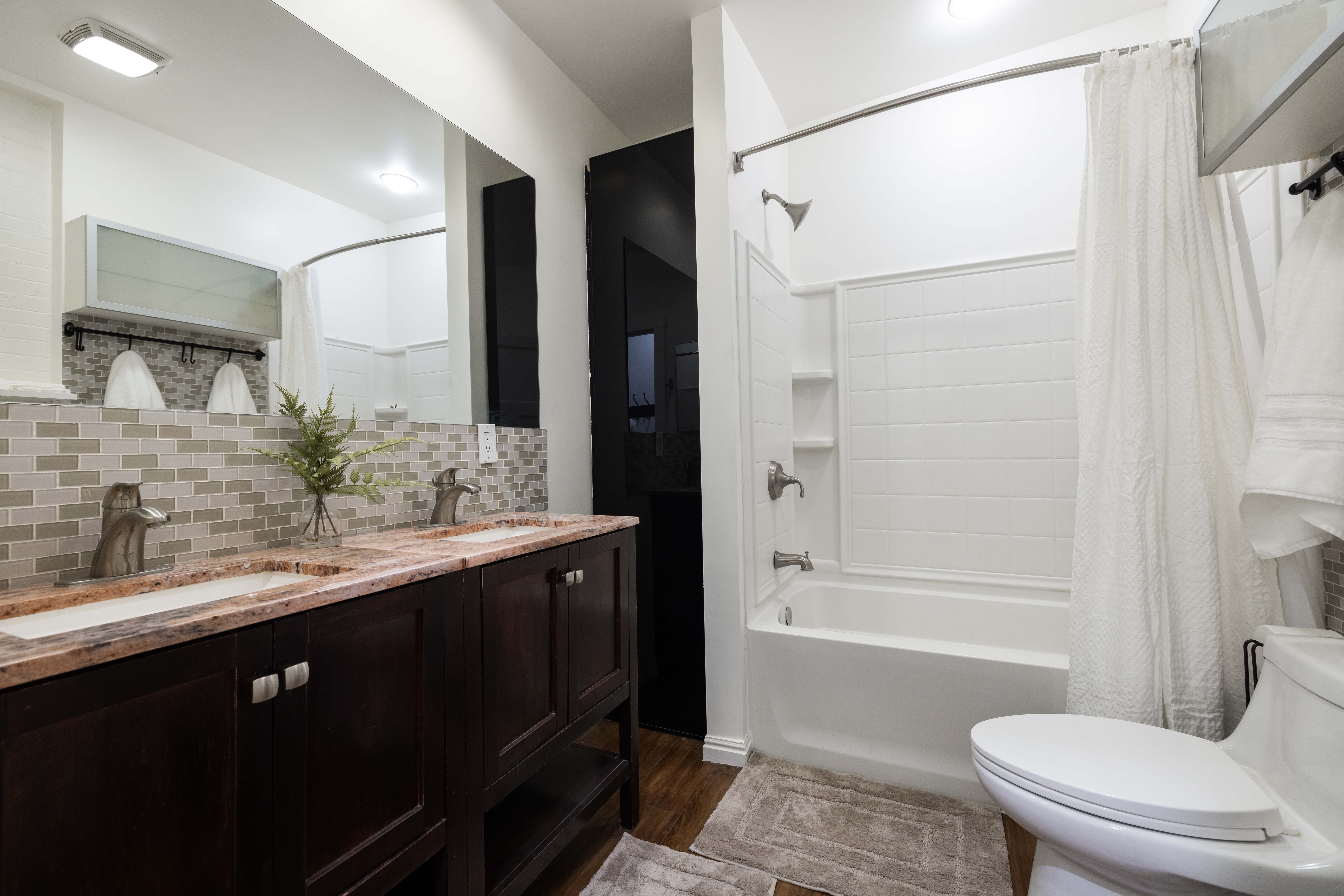 Apt. #1 Bathroom with double vanity, tiled backsplash, and dark wood-style floors