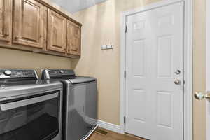 Laundry room with separate washer and dryer, light wood-type flooring, and cabinet space