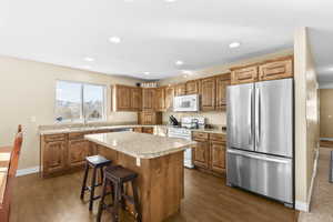 Kitchen with white appliances, light countertops, a breakfast bar, wood finish cabinetry, and a center island
