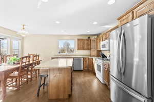 Kitchen with stainless steel appliances, dark wood-type flooring, wood finish cabinets, and decorative light fixtures