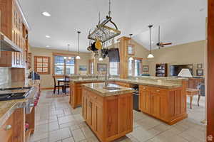 Kitchen featuring brown cabinetry, open floor plan, gas range, pendant lighting, and high vaulted ceiling