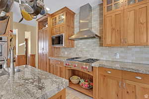 Kitchen with glass insert cabinets, wall chimney exhaust hood, appliances with stainless steel finishes, tasteful backsplash, and open shelves