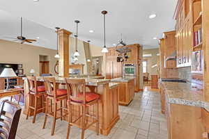 Kitchen featuring hanging light fixtures, a kitchen breakfast bar, brown cabinets, double oven, and under cabinet range hood