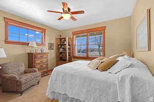 Bedroom with ceiling fan, light colored carpet, and multiple windows