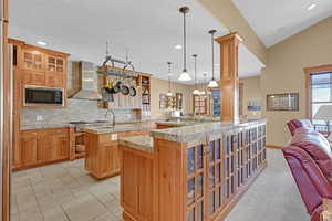 Kitchen featuring glass insert cabinets, pendant lighting, light stone countertops, a breakfast bar area, and wall chimney exhaust hood