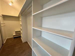 Large Walk in closet featuring dark colored carpet and vaulted ceiling