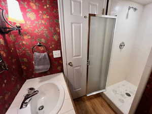 Bathroom with wallpapered walls, a shower stall, vanity, and wood finished floors