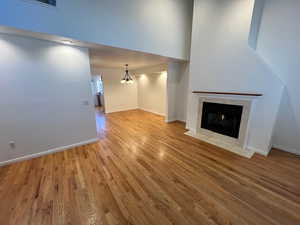 Unfurnished living room featuring light wood-type flooring, a fireplace, suspended lighting, and a high ceiling