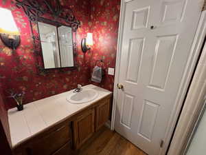 mainfloor bathroom with vanity, dark wood-style flooring, and wallpapered walls