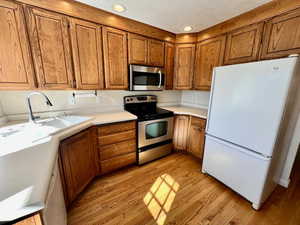 Kitchen featuring wood finish cabinetry, stainless steel appliances, light countertops, light wood finished floors, and recessed lighting