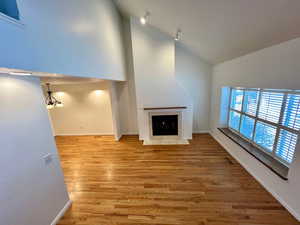 Unfurnished living room with light wood-type flooring, a tiled fireplace, and vaulted ceiling
