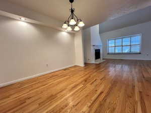 Unfurnished living room with light wood-type flooring, a chandelier, and a fireplace with flush hearth