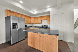 Kitchen with stainless steel appliances, a kitchen island, recessed lighting, dark countertops, and dark tile patterned floors