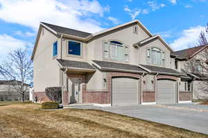 View of front facade with an attached garage, brick siding, concrete driveway, a front lawn, and stucco siding