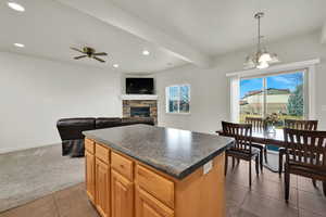 Kitchen featuring a stone fireplace, dark countertops, open floor plan, a kitchen island, and wood finish cabinetry