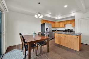 Kitchen featuring stainless steel appliances, suspended lighting, a center island, dark tile patterned flooring, and beam ceiling