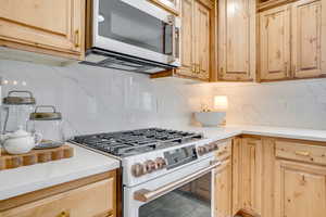 Kitchen with high end stove, tasteful backsplash, and light wood finish cabinetry