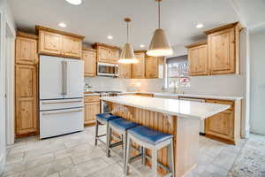 Kitchen featuring light wood finish cabinetry, stainless steel appliances, backsplash, and decorative light fixtures