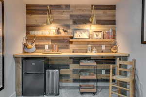 Indoor bar with freestanding refrigerator, wooden counters, wooden walls, and carpet floors