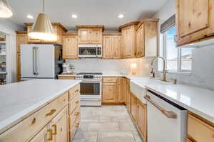 Kitchen featuring light wood finish cabinetry, decorative backsplash, white appliances, hanging light fixtures, and light stone counters
