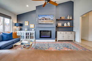 Living room featuring a large fireplace, ceiling fan, arched walkways, and wooden walls