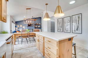 Kitchen with light wood finish cabinets, vaulted ceiling, hanging light fixtures, light tile patterned floors, and a kitchen bar