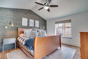 Bedroom featuring wood walls, an accent wall, wood finished floors, and a ceiling fan