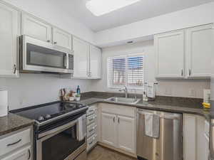 Kitchen featuring stainless steel appliances, white cabinets, and dark stone counters