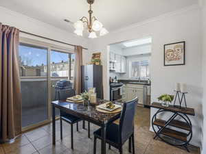 Dining room with a chandelier, dark tile patterned flooring, and ornamental molding