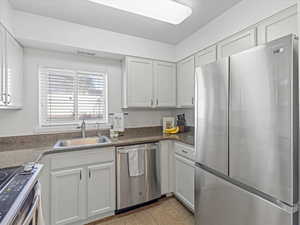 Kitchen with stainless steel appliances, white cabinetry, light tile patterned floors, and dark stone counters