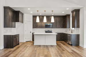 Kitchen with pendant lighting, a kitchen island, stainless steel appliances, dark wood finish cabinetry, and light wood finished floors