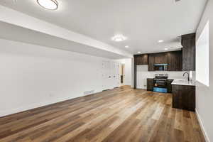 Kitchen with dark wood finish cabinetry, light countertops, electric stove, open floor plan, and light wood-style flooring