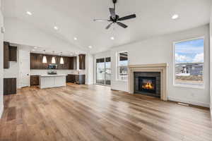 Unfurnished living room featuring a glass covered fireplace, recessed lighting, vaulted ceiling, light wood-style flooring, and a ceiling fan