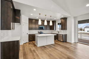 Kitchen featuring dark wood finish cabinets, decorative light fixtures, a kitchen island, tasteful backsplash, and lofted ceiling