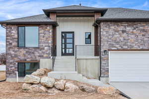 View of front of property featuring stone siding, a shingled roof, and concrete driveway