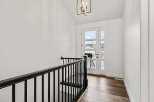 Hall featuring wood finished floors, vaulted ceiling, a chandelier, and an upstairs landing