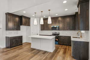 Kitchen featuring hanging light fixtures, stainless steel appliances, dark wood finish cabinetry, and backsplash