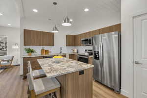 Kitchen featuring wood finish cabinetry, light stone countertops, stainless steel appliances, decorative light fixtures, and modern cabinets