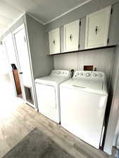 Laundry area featuring light wood-type flooring, washing machine and clothes dryer, cabinet space, and wooden walls