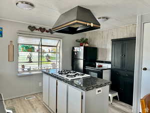 Kitchen with extractor fan, light wood-style flooring, wooden walls, a kitchen island, and black appliances