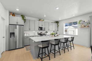 Kitchen with stainless steel appliances, gray cabinetry, a center island, and light wood finished floors